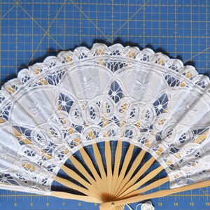 May include: A white lace fan with a wooden handle. The fan is closed and the lace is intricate and delicate.