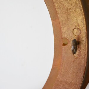 May include: A gold-coloured round frame with a keyhole and two small holes on the side. The frame has a decorative edge.