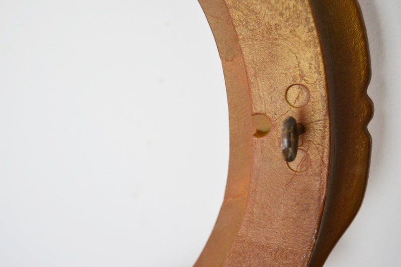 May include: A gold-coloured round frame with a keyhole and two small holes on the side. The frame has a decorative edge.