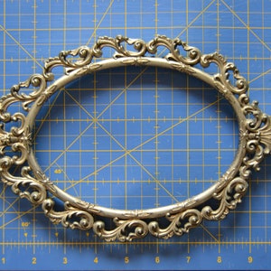 May include: A gold-colored ornate oval picture frame with a decorative, scrolled design.