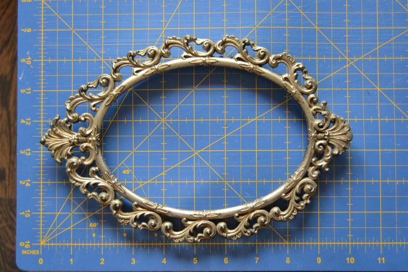 May include: A gold-colored ornate oval picture frame with a decorative, scrolled design.