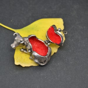May include: A silver cow-shaped trinket box with a red velvet interior. The box is open and the lid is propped up on a yellow leaf.