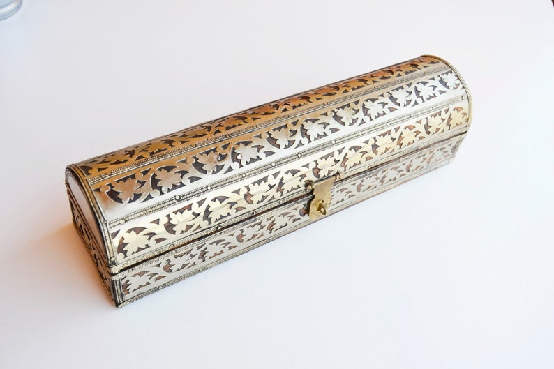 May include: A silver and gold decorative box with an ornate floral design. The box has a hinged lid and a brass lock.
