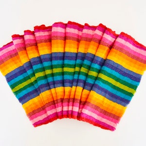 May include: A set of rainbow striped fabric napkins folded in a fan shape. The napkins are made of a soft, woven fabric and feature a variety of colours, including red, orange, yellow, green, blue, indigo, and violet.