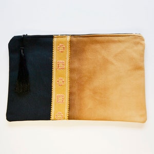 May include: A black and tan fabric clutch with a gold embroidered trim and a black tassel.