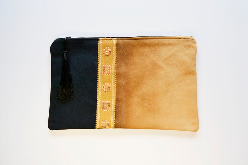 May include: A black and tan fabric clutch with a gold embroidered trim and a black tassel.