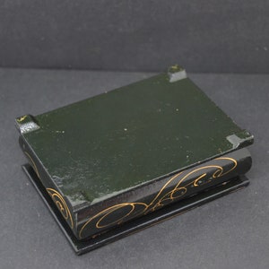 May include: A small black wooden box with gold painted designs. The box has a hinged lid and is closed.