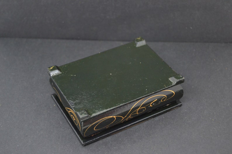 May include: A small black wooden box with gold painted designs. The box has a hinged lid and is closed.