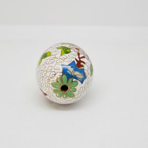 May include: White egg-shaped ornament with a floral design in shades of green, blue, red, and gold. The ornament has a small hole at the top.