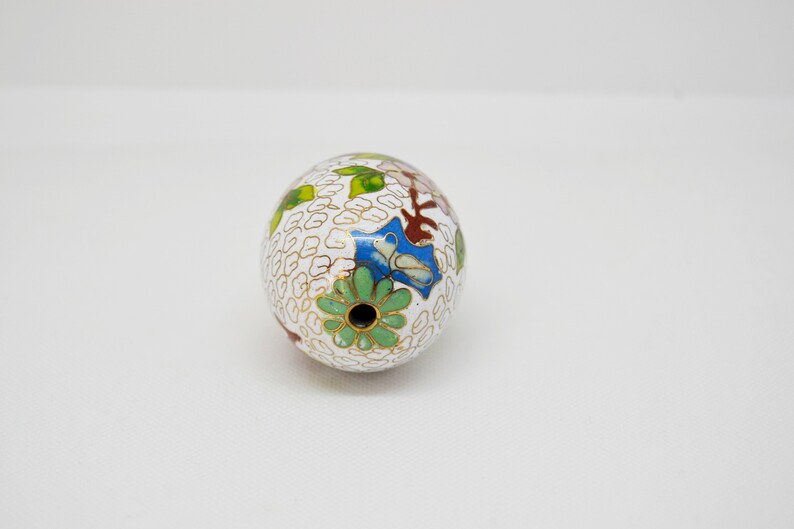 May include: White egg-shaped ornament with a floral design in shades of green, blue, red, and gold. The ornament has a small hole at the top.