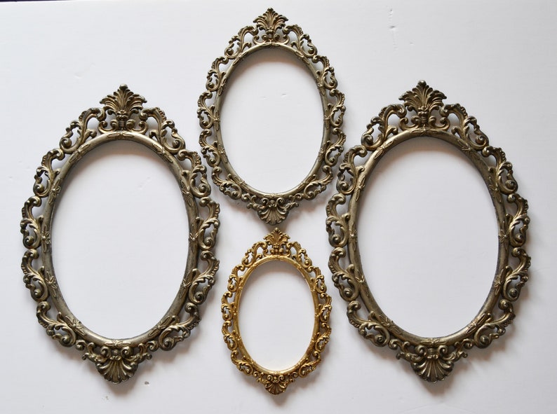 May include: Four ornate oval picture frames, three are silver and one is gold. The frames are all different sizes and have intricate designs.