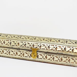 May include: A long, rectangular box with a curved top. The box is made of wood and has intricate silver and gold floral designs carved into the surface. The box has a brass latch.