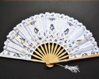 May include: A white lace fan with a wooden handle and a white tassel. The fan is closed and the lace is intricate.