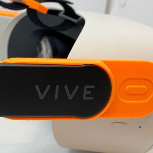 May include: A black and orange VR headset strap with the word "VIVE" printed on it.