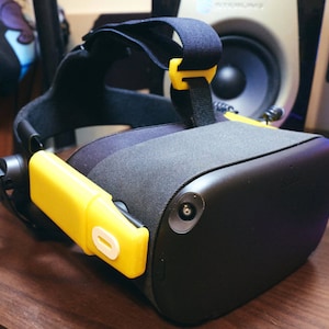 May include: A black virtual reality headset with a yellow and white strap and a yellow and white side strap. The headset has a black fabric covering the top and a black plastic front.