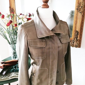 May include: A brown leather jacket with white stitching and a collar that can be worn up or down. The jacket has two pockets on the front and a button closure.