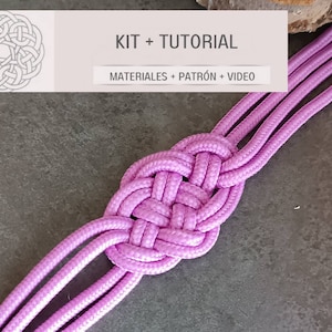 Könnte beinhalten: Nahaufnahme eines geflochtenen Armbands in Pink mit einem Knoten in der Mitte. Das Armband besteht aus drei Schnüren und hat einen silbernen Verschluss. Der Text "KIT + TUTORIAL" ist über dem Armband sichtbar.