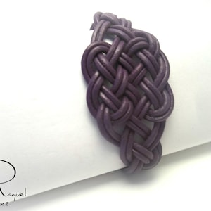 May include: A purple leather bracelet with a woven knot design.