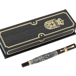 Puede incluir: Un bolígrafo negro con detalles dorados y un diseño plateado con un escudo de armas. El bolígrafo viene en una caja de cuero negro con ribetes dorados y un escudo de armas dorado.