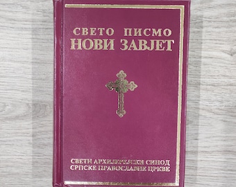 May include: A burgundy-colored book with gold lettering and a gold cross emblem. The text on the cover reads "СВЕТО ПИСМО НОВИ ЗАВЈЕТ" and "СВЕТИ АРХИЈЕРЕЈСКИ СИНОД СРПСКЕ ПРАВОСЛАВНЕ ЦРКВЕ". The book is rectangular and appears to be a religious text.