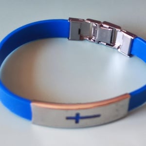 Puede incluir: Pulsera de silicona azul con cierre de acero inoxidable y placa metálica decorativa. La placa presenta un símbolo de cruz azul. Un accesorio sencillo y elegante.