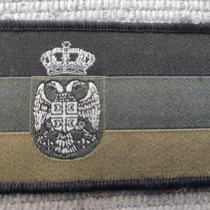 Op de afbeelding: Een geborduurde patch in zwart, groen en goud met het wapen van Servië. Het wapen toont een dubbelkoppige adelaar met een kroon bovenop.