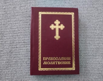 May include: A burgundy leather-bound prayer book with a gold cross and the text "Православный молитвоник" on the front cover.