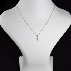 Pode incluir: Um colar de corrente de prata com um pequeno pingente de anjo.