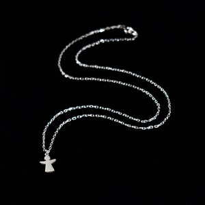 Pode incluir: Um colar de corrente de prata com um pequeno pingente de anjo. A corrente &eacute; delicada e o anjo tem um design simples.