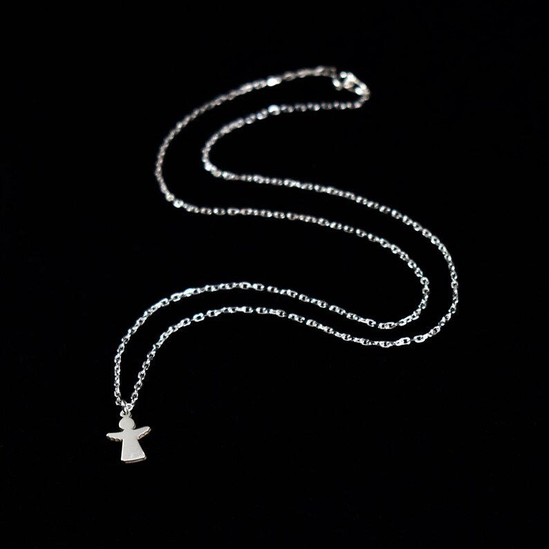 Pode incluir: Um colar de corrente de prata com um pequeno pingente de anjo. A corrente &eacute; delicada e o anjo tem um design simples.