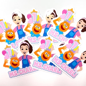 May include: A collection of colorful stickers featuring a cartoon woman, an orange monster, and the number 1. The woman wears a pink shirt and blue overalls. The monster has orange fur and a blue shirt. The stickers have the text "MS. CHARLI".