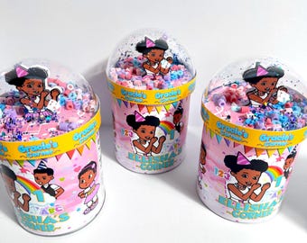 May include: Three clear plastic containers filled with colorful beads and confetti. Each container has a lid and a label with the text "Gracie's Corner" and a cartoon illustration of a girl. The containers are on a white surface.