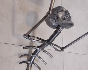 Puede incluir: Un portarrollos de papel higiénico de metal hecho a mano con un diseño único. Presenta una figura esquelética con una calavera, brazos y caja torácica, sosteniendo un rollo de papel higiénico. El soporte está montado sobre una base de metal con pernos.
