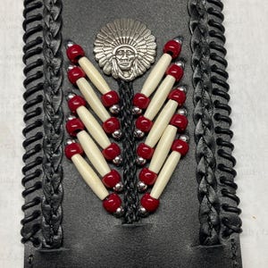 Peut inclure: Accessoire de moto en cuir noir avec bords tressés et perles décoratives. Comprend un emblème de coiffe amérindienne argenté et un motif de perles rouges et blanches.