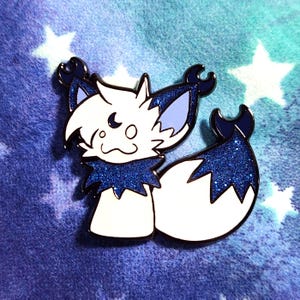 May include: A white and blue enamel pin featuring a stylized fox-like creature with a crescent moon detail. The pin has a glittery blue collar and tail, with black outlines. The background is a blue and teal gradient with white star shapes.