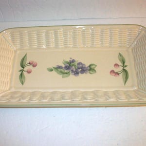 May include: Rectangular ceramic serving dish with a cream-colored background and a woven basket design on the sides. The center features a floral design with purple flowers and cherries.