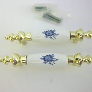 May include: Two cabinet pulls with white ceramic centers featuring blue floral designs. The ends and hardware are gold-toned. A small packet of screws is included.
