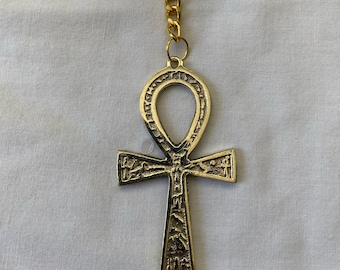 Pode incluir: Um chaveiro Ankh dourado com um design detalhado. O Ankh é um símbolo da vida eterna na mitologia egípcia antiga.