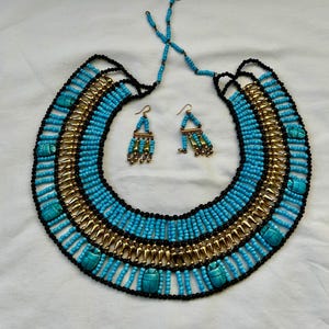 Peut inclure: Un ensemble collier et boucles d'oreilles de style égyptien. Le collier est un large collier avec des perles turquoise, des accents noirs et des détails en métal doré. Les boucles d'oreilles sont pendantes avec des éléments turquoise et dorés.
