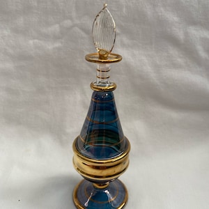 May include: A blue glass perfume bottle with gold accents and a clear glass stopper. The bottle has a round base and a pear-shaped body.