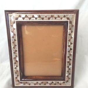 May include: A rectangular wooden picture frame with a dark brown finish. The frame is decorated with a border of small, triangular mother-of-pearl inlays. The interior has a light brown backing.