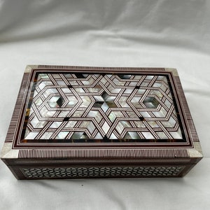 May include: A wooden box with a geometric pattern inlaid with mother of pearl. The box has a dark brown wood frame and a light brown wood interior.