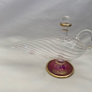 May include: A clear glass genie bottle with a gold-rimmed stopper and a pink base. The bottle has a swirling design and a handle.