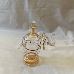 May include: A clear glass bottle shaped like an elephant with gold accents. The bottle has a stopper and is perfect for holding perfume or essential oils.