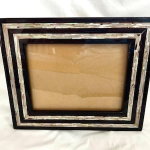May include: Rectangular photo frame with a black border and inlaid mother-of-pearl accents. The frame has a glossy finish and a brown backing. The design features a layered effect with alternating black and iridescent stripes.