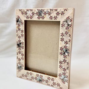 Può includere: Cornice fotografica rettangolare decorativa con un motivo a mosaico dettagliato. Il bordo della cornice presenta un motivo ripetuto di elementi a forma di stella in bianco, nero e rosso. La cornice è in legno e ha un retro di colore neutro.