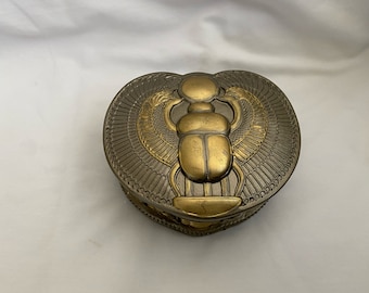 May include: A gold and silver metal trinket box shaped like a heart with a scarab beetle design.