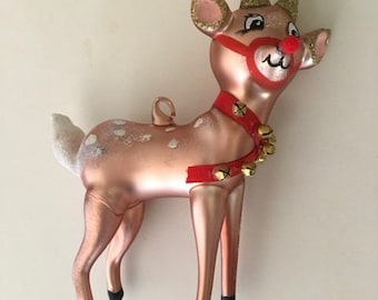 May include: A pink glass reindeer Christmas ornament with gold glitter, a red nose, and a red and gold jingle bell collar.
