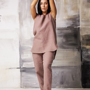 Op de afbeelding: Een vrouw draagt een mauve linnen broekpak met een top zonder mouwen en een bijpassende broek. Ze draagt zwarte sandalen met bandjes.