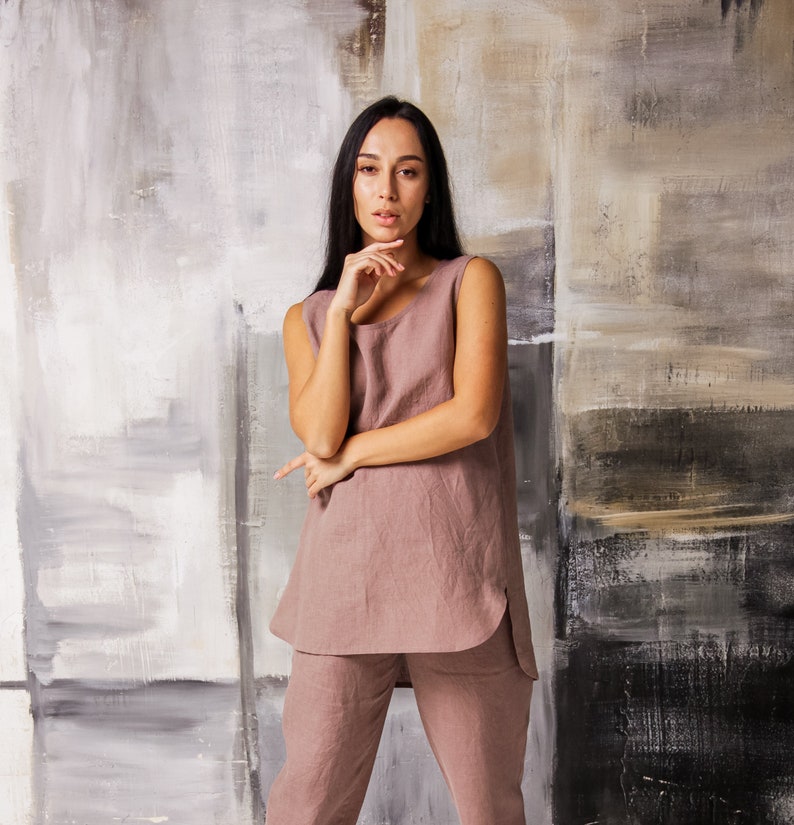 Op de afbeelding: Een vrouw draagt een mouwloos, stoffig roze linnen top en een bijpassende broek. De top heeft een ronde hals en een licht gebogen zoom. De broek heeft een ontspannen pasvorm en is net boven de enkels geknipt.